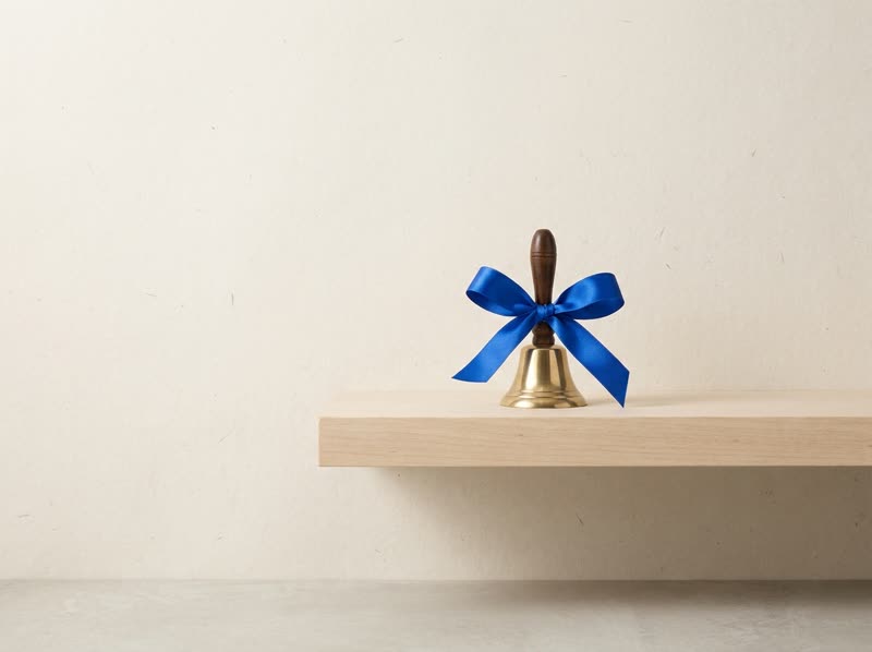 A small brass bell on a shelf with a single blue ribbon.